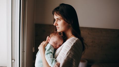A serene moment of a mother holding her sleeping baby near a window, indoors.