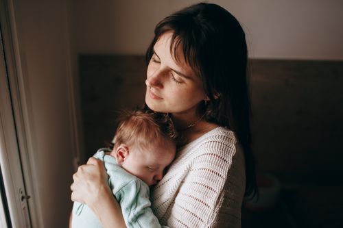 Free A serene indoor portrait of a mother holding her sleeping baby, illustrating love and tenderness. Stock Photo