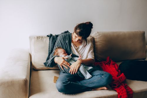 Free Tender moment of a mother holding her newborn baby on a cozy sofa, creating a heartfelt family scene. Stock Photo