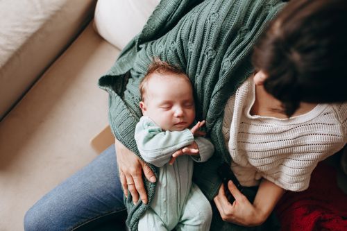 Free Tender moment of a mother holding her sleeping newborn at home, showcasing love and warmth. Stock Photo