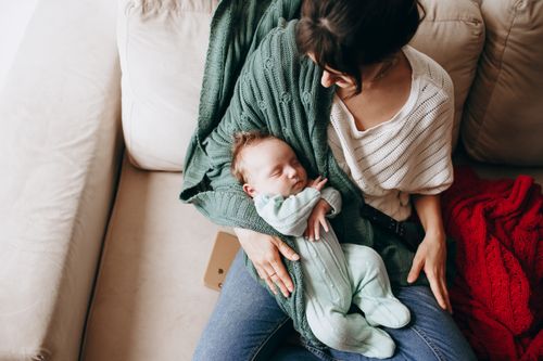 Free A tender moment of a mother lovingly holding her sleeping baby indoors. Stock Photo