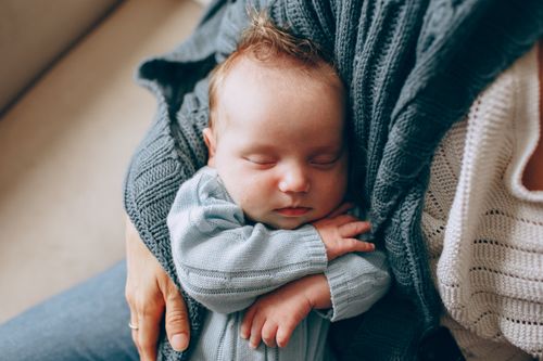 Free A serene and cute portrait of a newborn baby sleeping peacefully, cradled in a parent's arms. Stock Photo