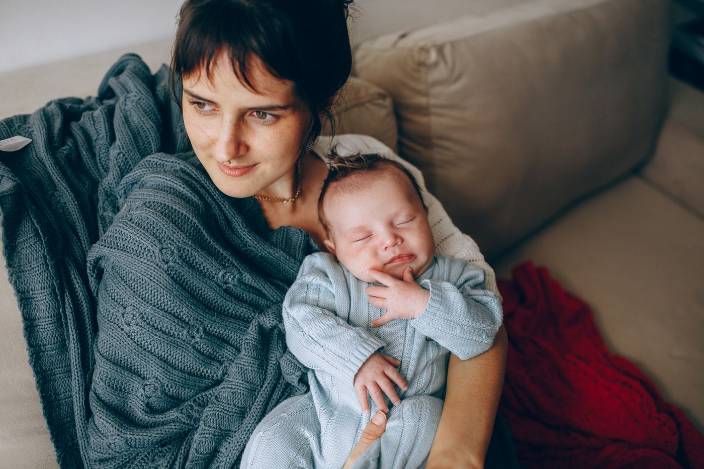 Awake mother seated on a sofa holding her baby close in her arms