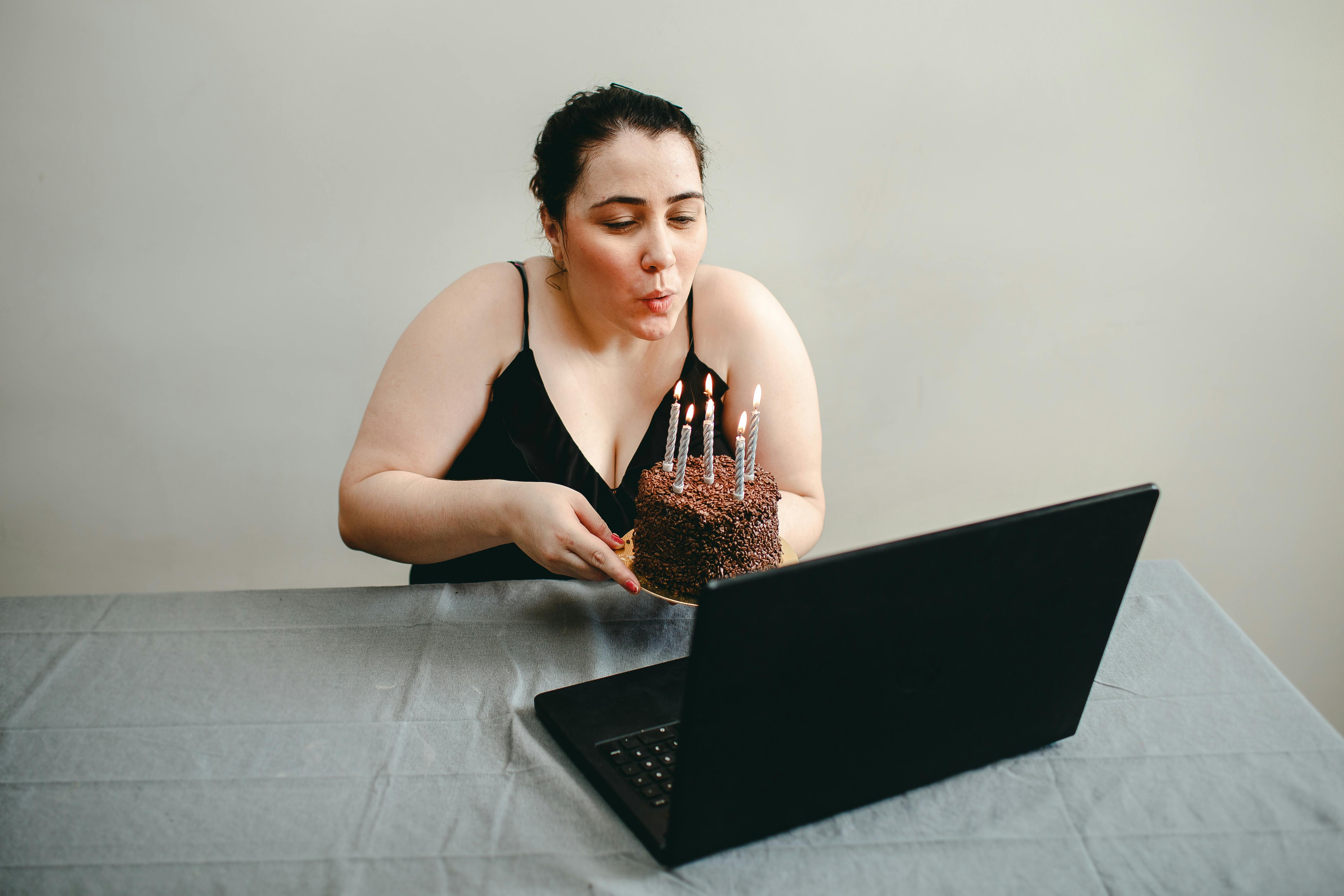 woman sitting and holding birthday cake in front of laptop