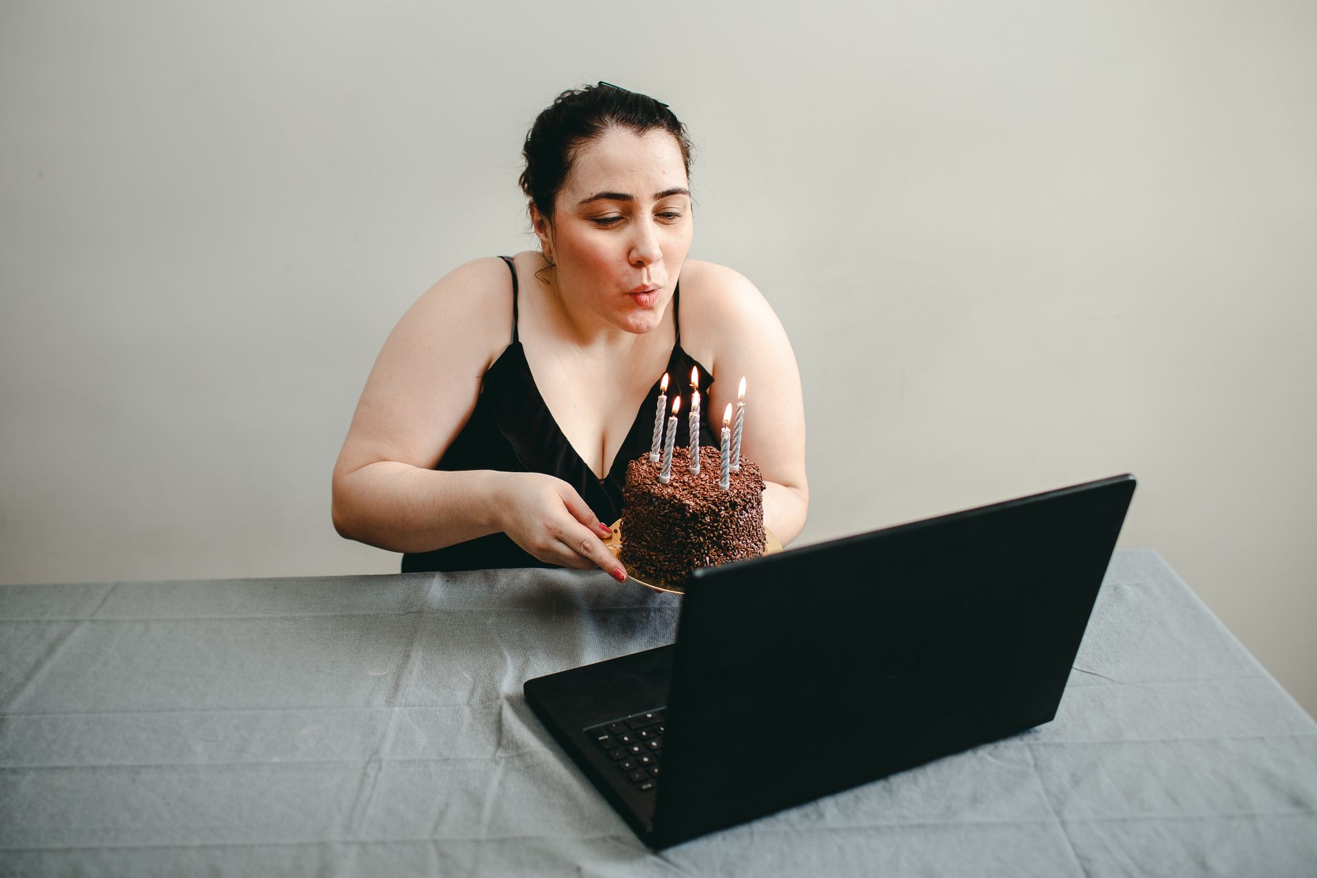 Woman blowing candles on cake during a virtual birthday celebration via laptop.