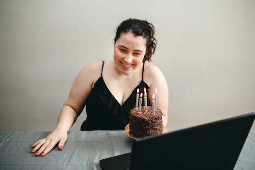 Woman smiling at laptop during her virtual birthday celebration with a chocolate cake.