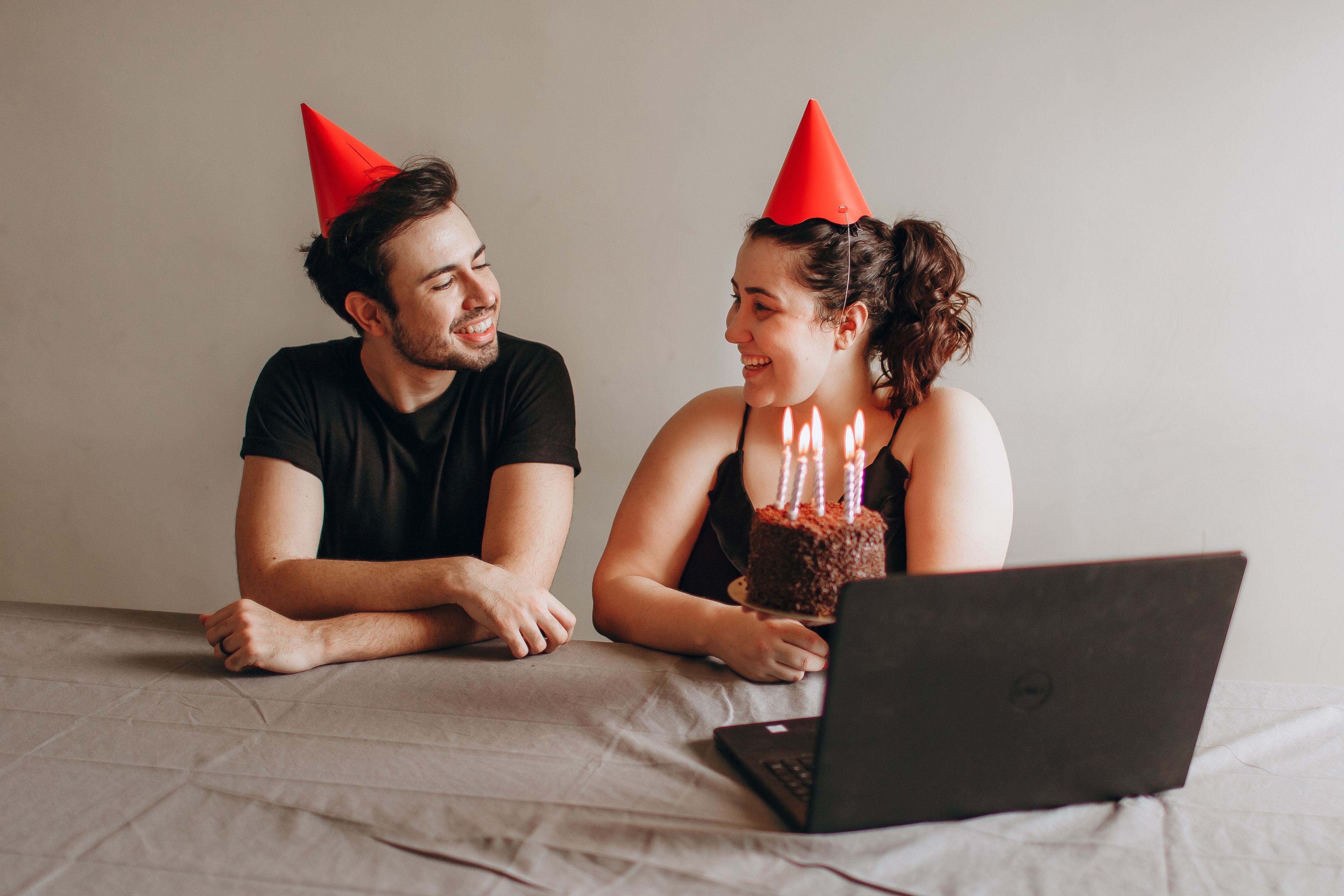 Two friends celebrate a birthday with a chocolate cake and hats in a virtual setting.