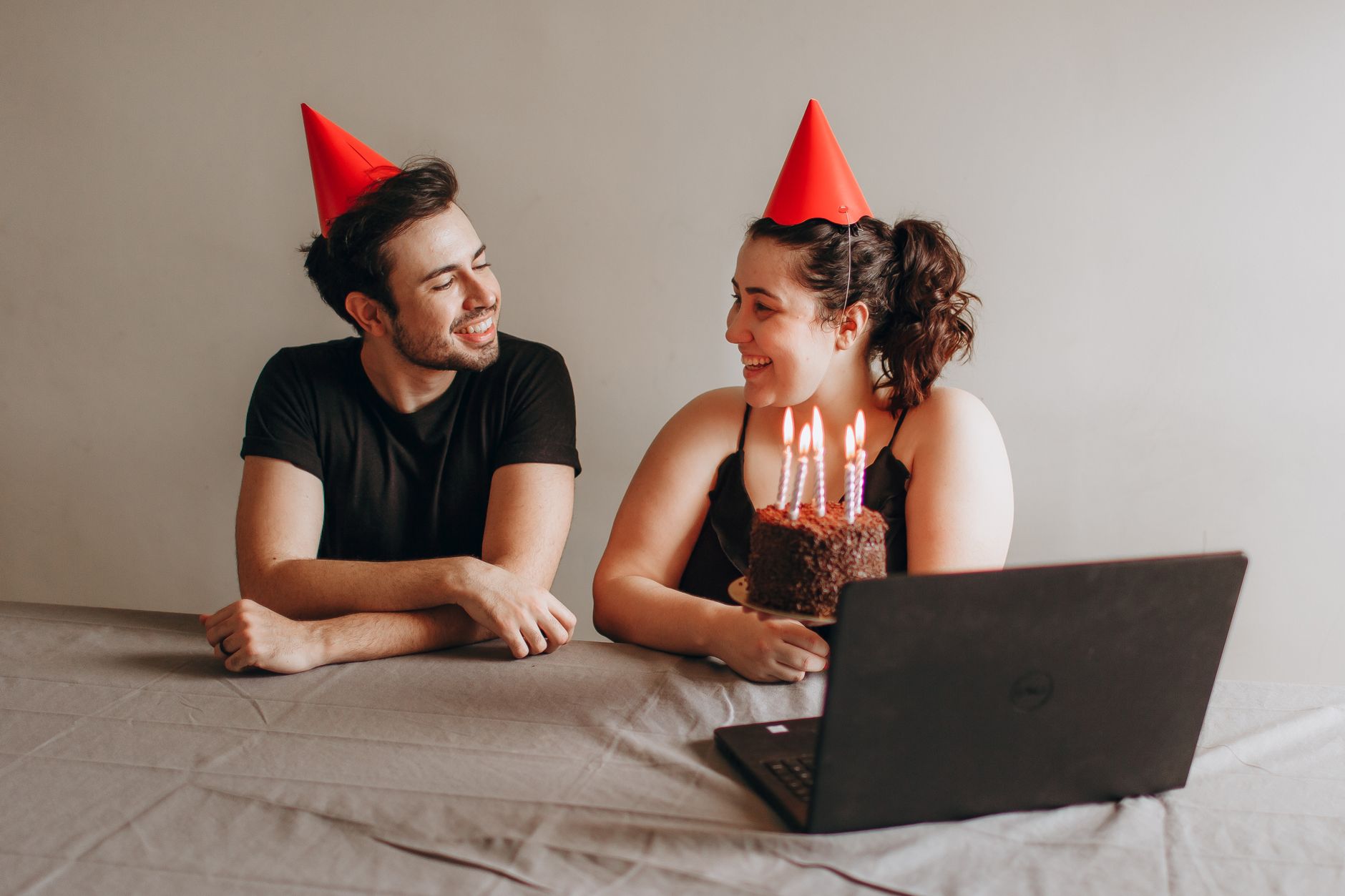 Two friends celebrate a birthday with a chocolate cake and hats in a virtual setting.