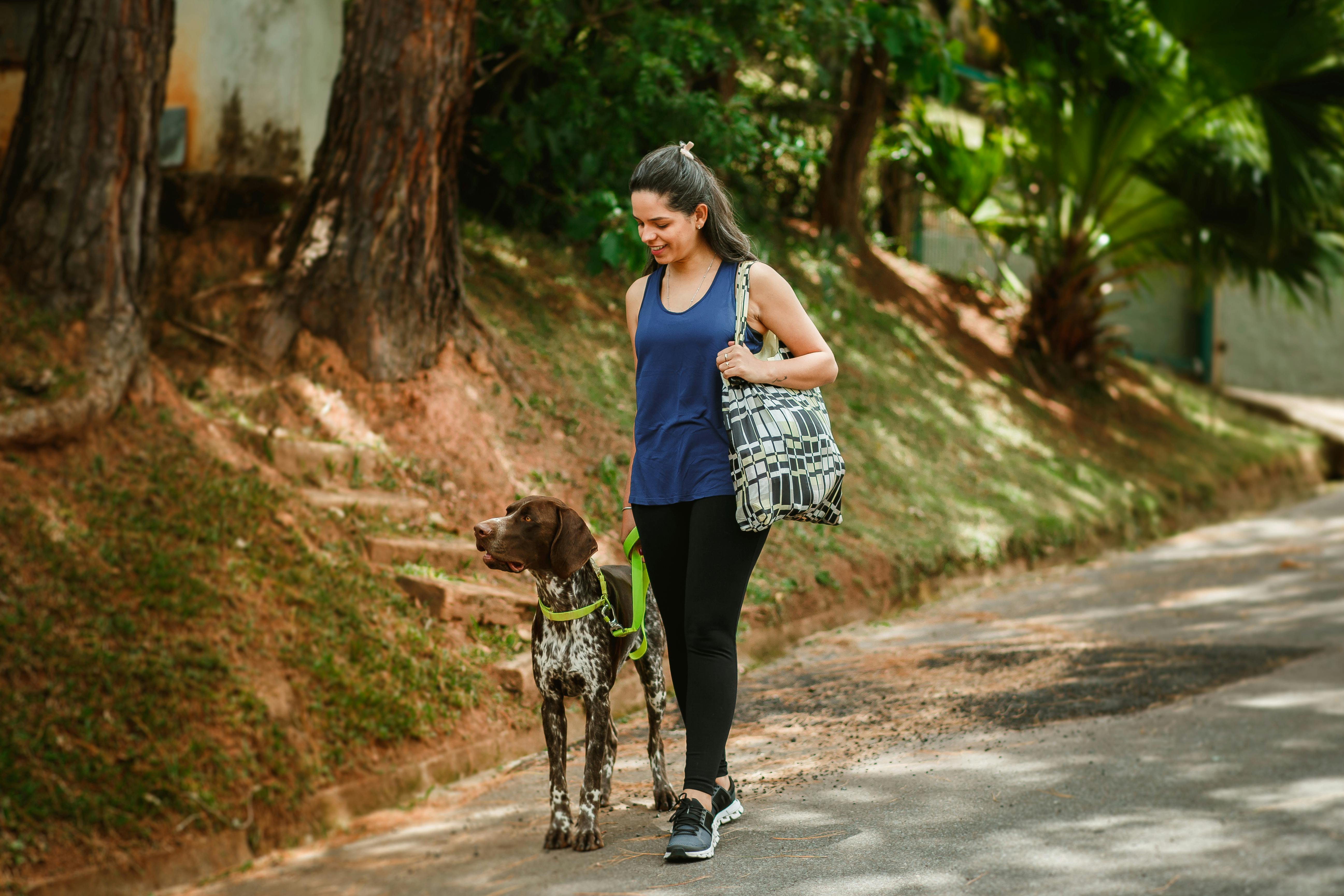 A woman strolls with her dog on a sunny day, embodying outdoor leisure and companionship.