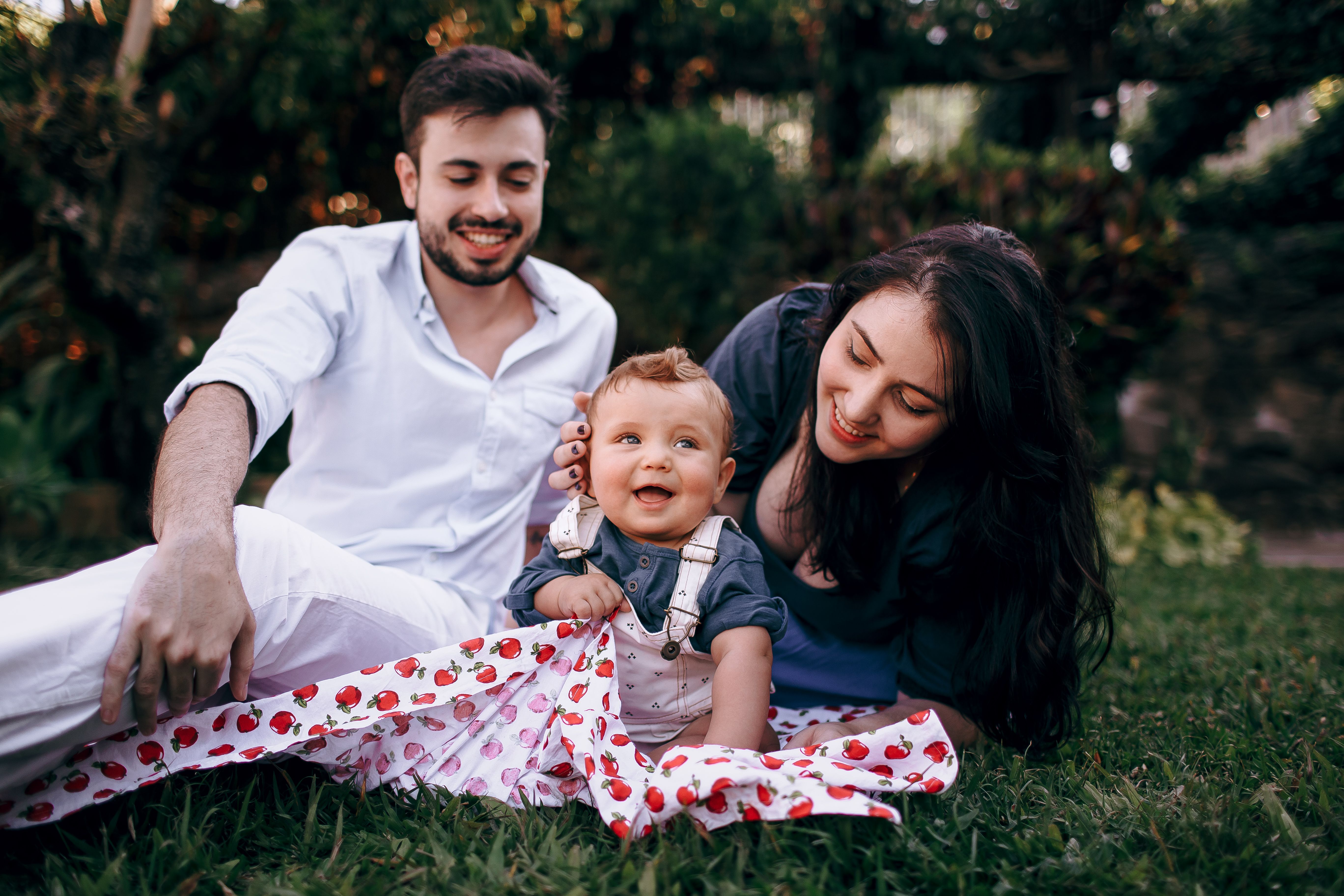 Smiling family with a baby enjoying a sunny day picnic outdoors, surrounded by nature.