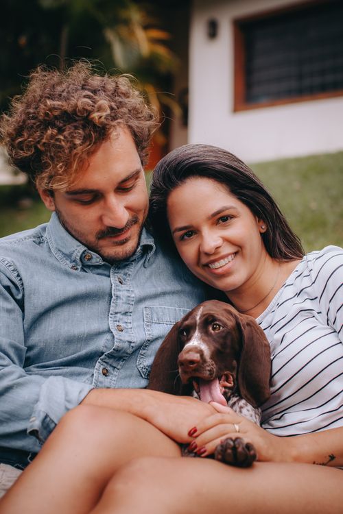 Free Smiling couple cuddling a puppy outdoors on a bright day, showcasing joy and companionship. Stock Photo