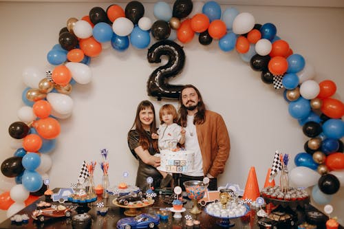 Family celebrating a child's birthday with balloons and cake in home