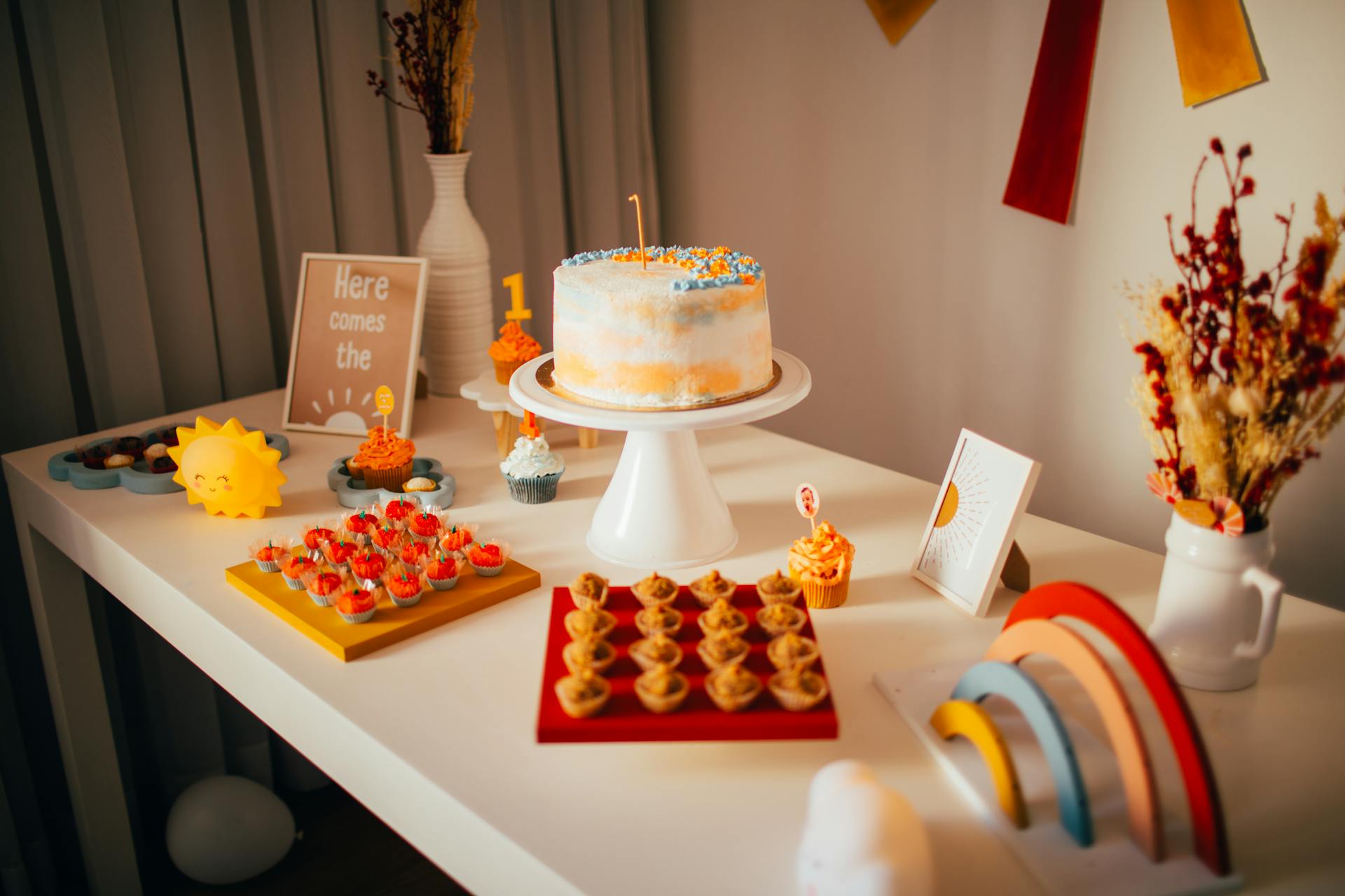 Colorful first birthday party table setup with cake and decorations indoors.