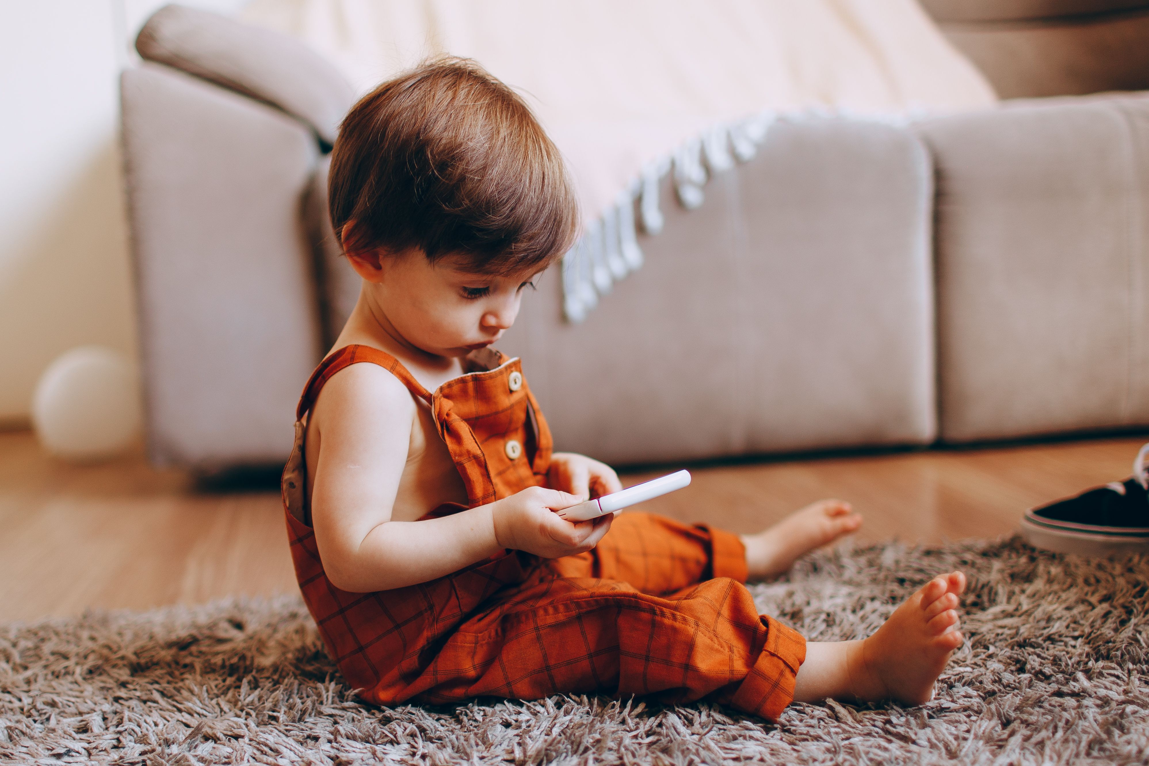 A toddler sitting on the floor playing with a cell phone · Free Stock Photo