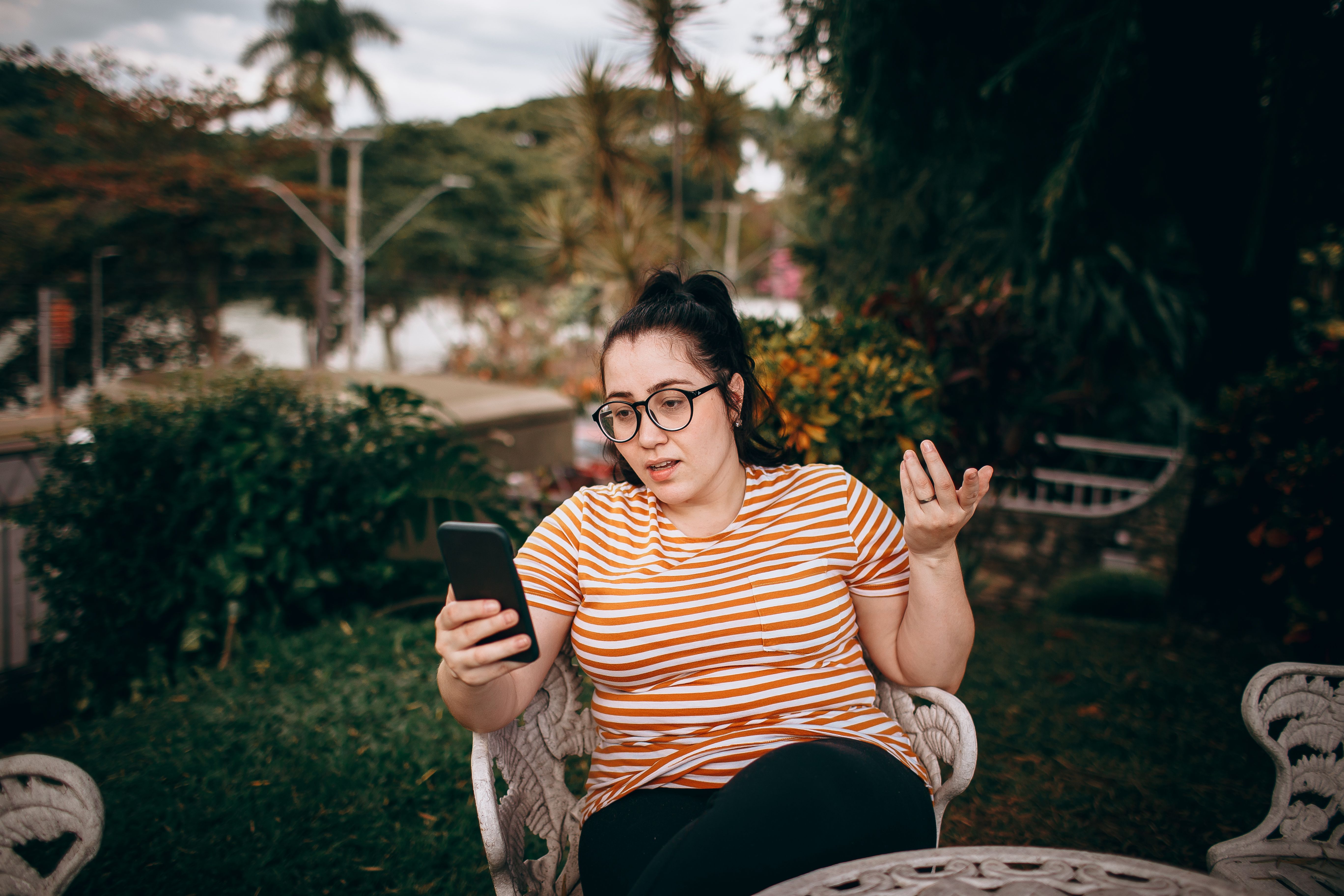 person holding a phone with a cracked screen, sitting alone on a park bench, looking exhausted