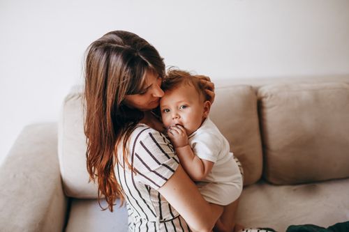 Free A tender moment between a mother and her baby, expressing love and warmth on a cozy home sofa. Stock Photo