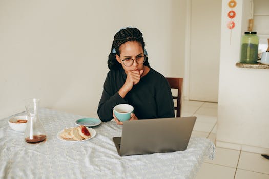 A woman sitting at a table with coffee, engaging in work from her laptop.