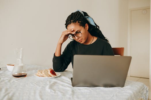 Focused woman using laptop at home with coffee and breakfast on table.