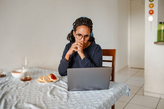 Adult woman concentrated on laptop work with breakfast beside. Indoor home setting of relaxed working atmosphere.