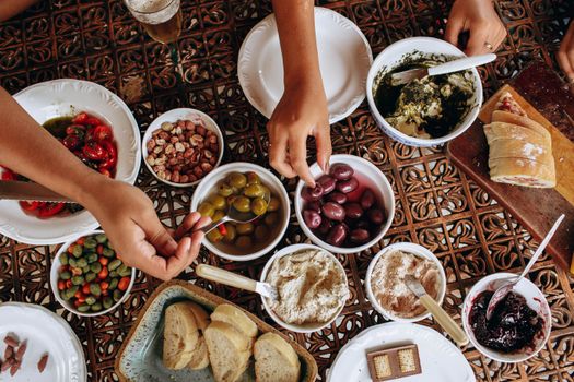 Overhead view of a rustic Mediterranean meal setup with diverse dishes and hands reaching.