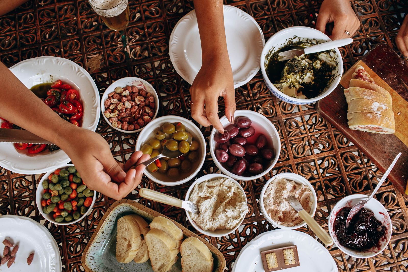 Overhead view of a rustic Mediterranean meal setup with diverse dishes and hands reaching.