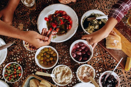 A lively Mediterranean meal with various dishes, showcasing hands reaching for olives and bread.