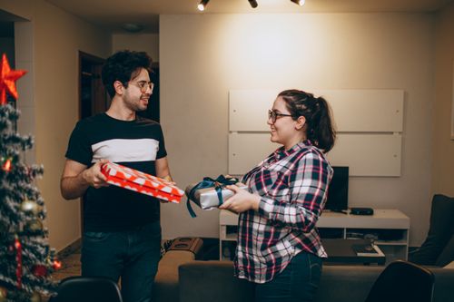 Free A cheerful moment of a couple exchanging gifts in their cozy living room decorated for Christmas. Stock Photo