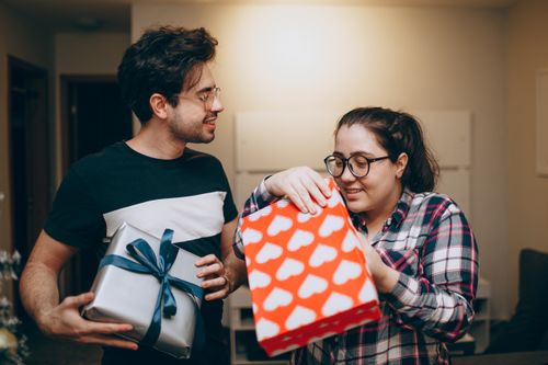 Free A joyful couple exchanges presents indoors, enjoying a heartwarming moment together. Stock Photo