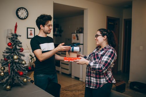 Free A happy man and woman exchanging gifts near a decorated Christmas tree inside a cozy home. Stock Photo