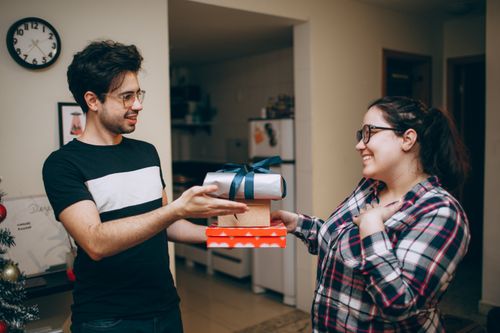 Free A couple happily exchanging Christmas gifts in a cozy indoor setting, capturing the joy of the holiday season. Stock Photo