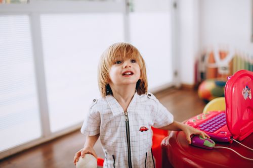 Free Smiling blond child enjoying playtime with a toy laptop indoors. Stock Photo