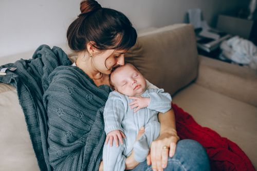 Free A mother lovingly holds her sleeping baby on a cozy sofa, wrapped in warmth and affection. Stock Photo