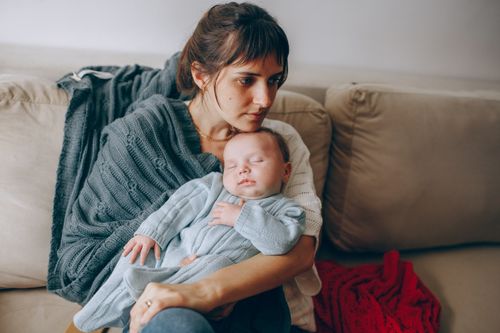 Free A peaceful moment as a mother holds her sleeping baby on a cozy couch. Stock Photo