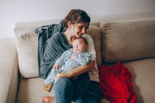 Free A tender moment of a mother cradling her sleeping baby on a cozy sofa. Stock Photo