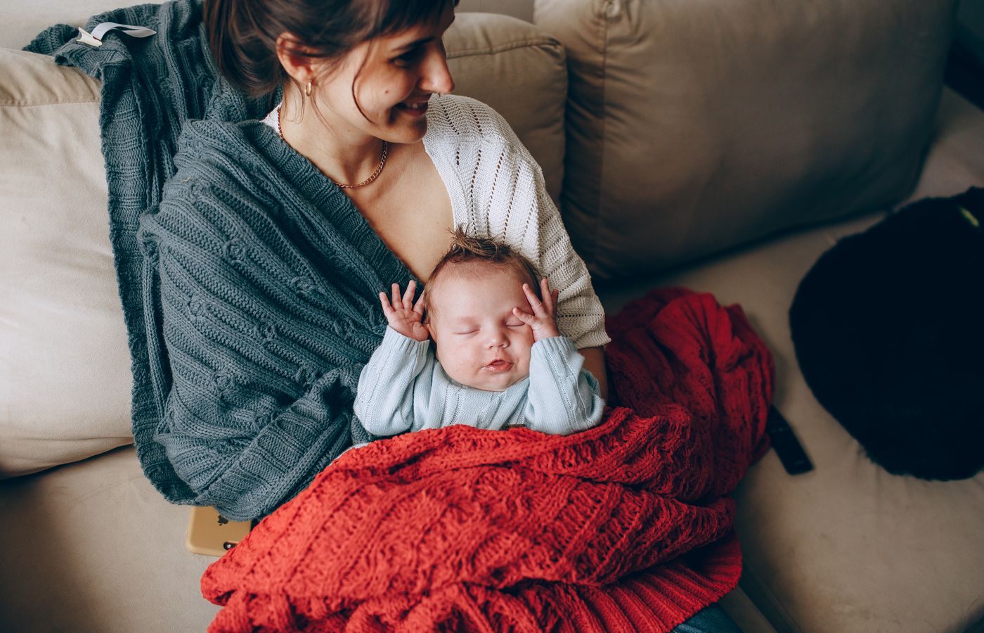 A tender moment of a mother holding her sleeping baby wrapped in a warm blanket indoors.