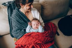 A tender moment of a mother holding her sleeping baby wrapped in a warm blanket indoors.