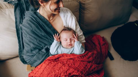 A tender moment of a mother holding her sleeping baby wrapped in a warm blanket indoors.
