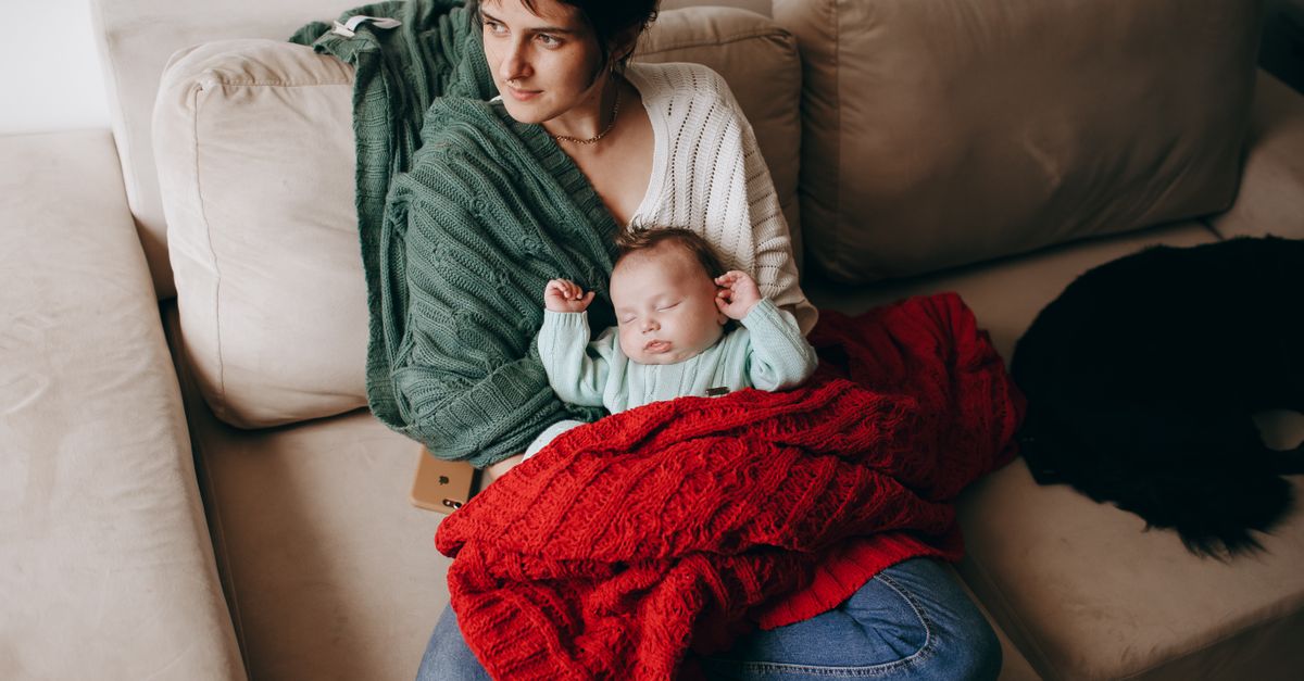 A mother lovingly holding her baby on a cozy sofa, wrapped in warm blankets.