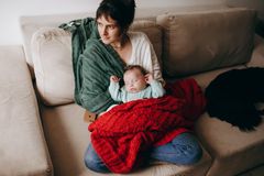 A mother lovingly holding her baby on a cozy sofa, wrapped in warm blankets.