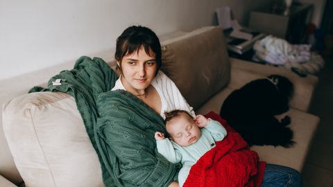 A mother lovingly holds her sleeping baby on a cozy sofa, surrounded by warm blankets.