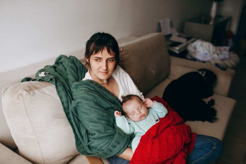Mãe segurando o bebê adormecido no sofá com cobertores