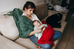 A mother lounges on a sofa with her sleeping baby, wrapped in blankets, creating a cozy family moment.