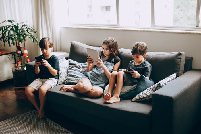 Three children engrossed in their phones and tablets on the sofa