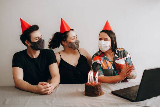 A diverse group enjoys a masked birthday celebration over video call indoors.