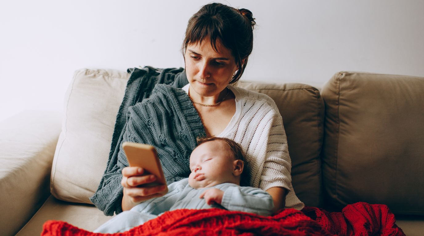スマートフォンで情報を確認する母親と眠る赤ちゃん