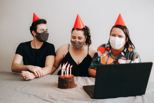 Three people wearing masks celebrate a birthday with a cake and a virtual call.