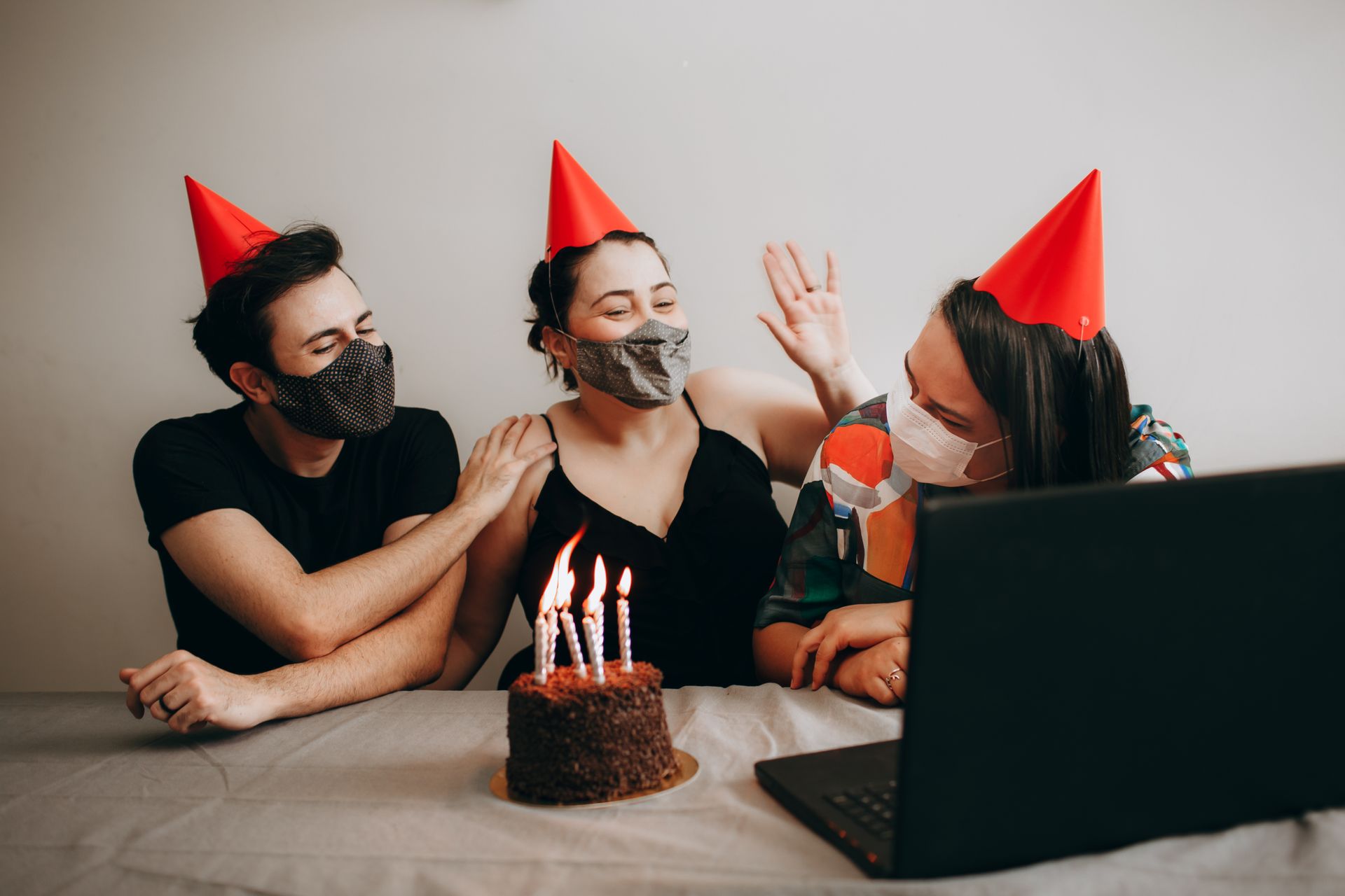 A joyful group of friends celebrating a birthday online with masks and a cake.