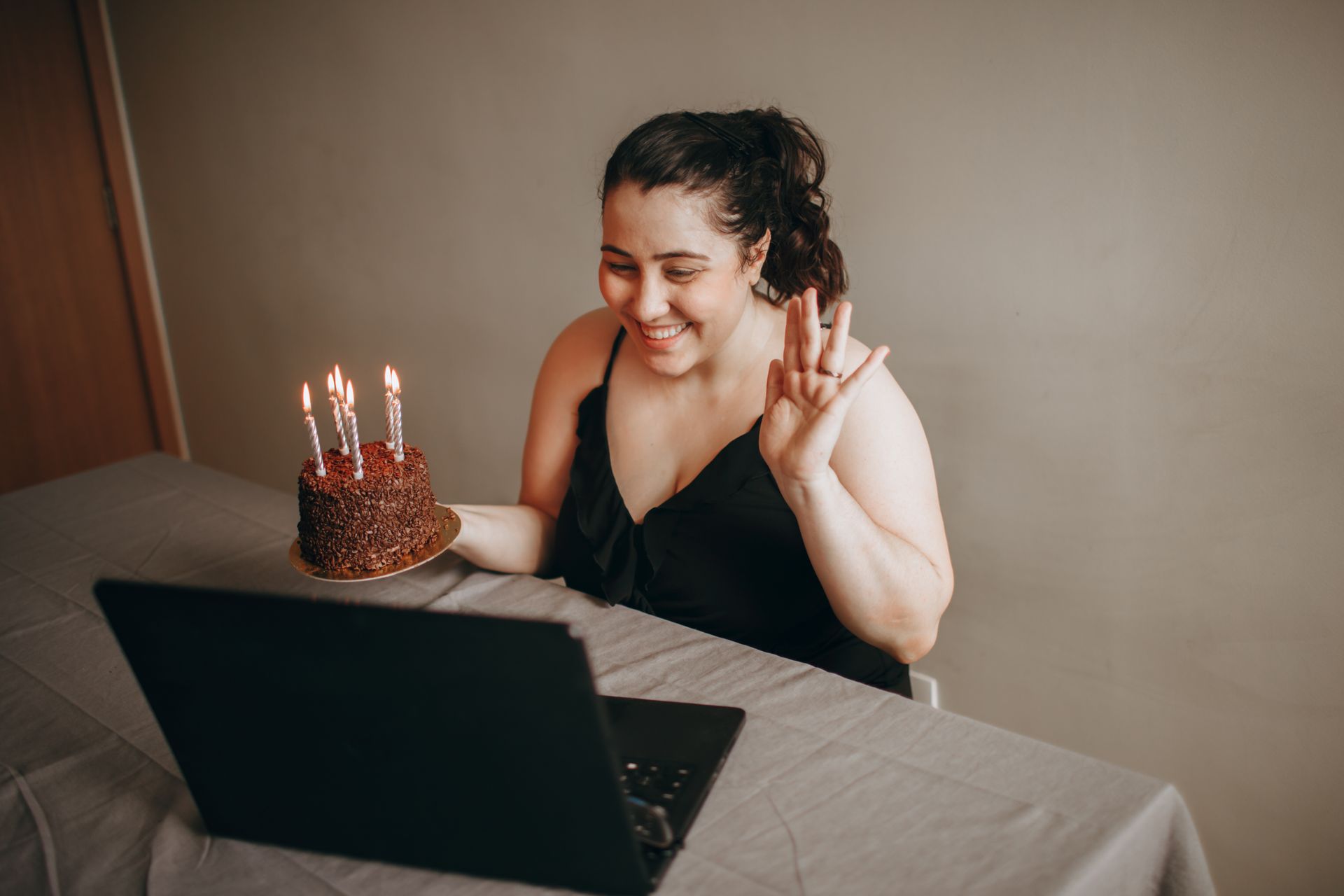 Smiling woman enjoying a virtual birthday party with a chocolate cake and candles.