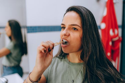 Free Woman brushing her teeth using a natural toothbrush in a bathroom, promoting oral hygiene and sustainability. Stock Photo