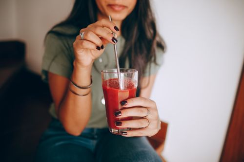 Free A woman enjoying a refreshing red juice indoors, stirring it with a straw. Stock Photo